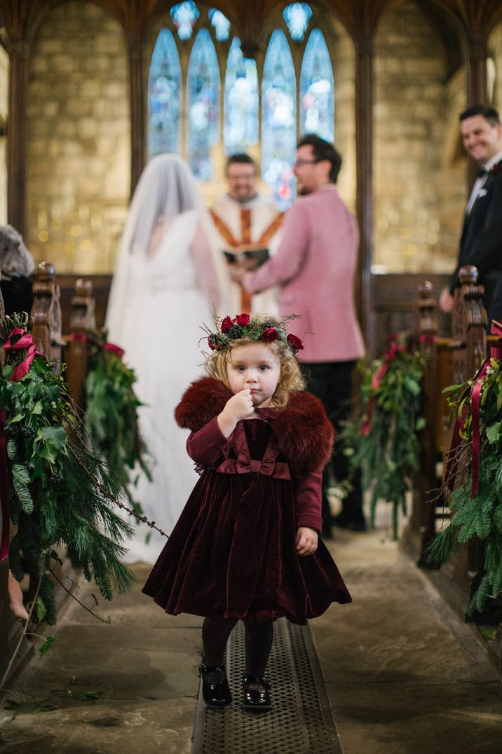 Cute flower girl at winter wedding in a burgundy velvet dress, tights and faux fur shawl 