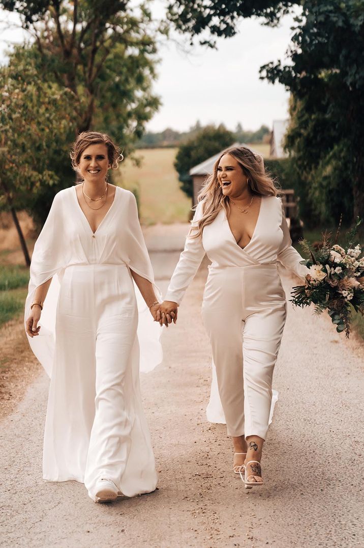 Two brides in a fitted satin jumpsuit and floaty wide leg jumpsuit at Cotswolds wedding 