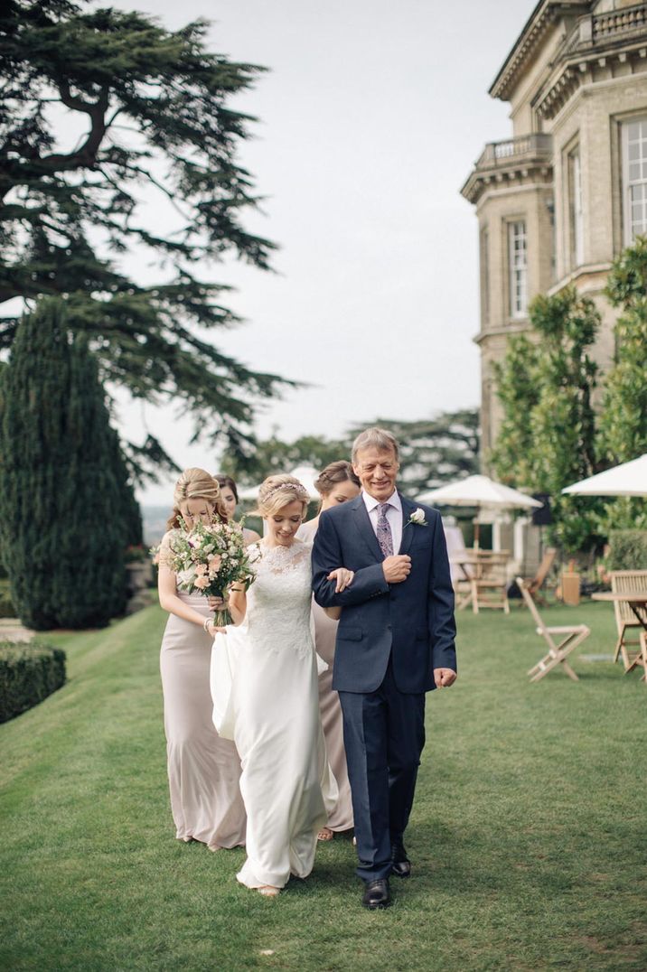 Groom in dark suit and bride in lace dress walking Hedsor Hall grounds