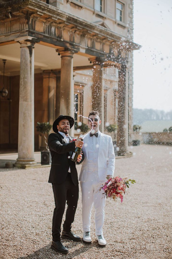 Grooms in white tux and black tux doing a champagne pop