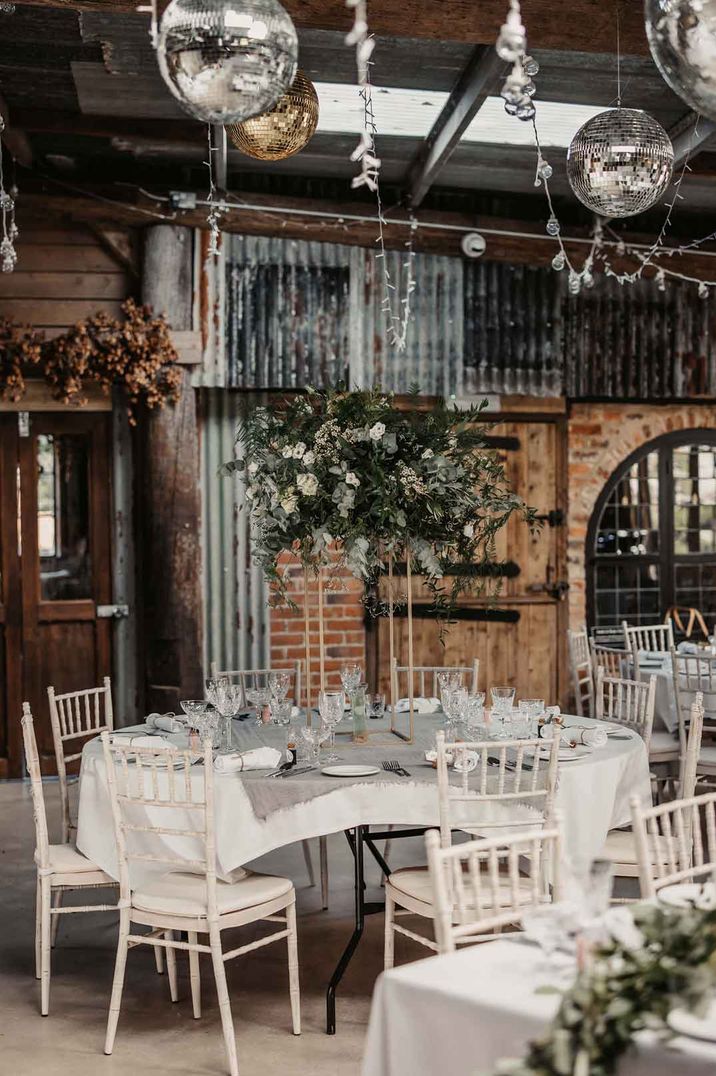 Rustic wedding tablescape at Oak Tree Barn with white wedding tablecloths, suspended foliage decor, hanging disco balls and fairy lights 