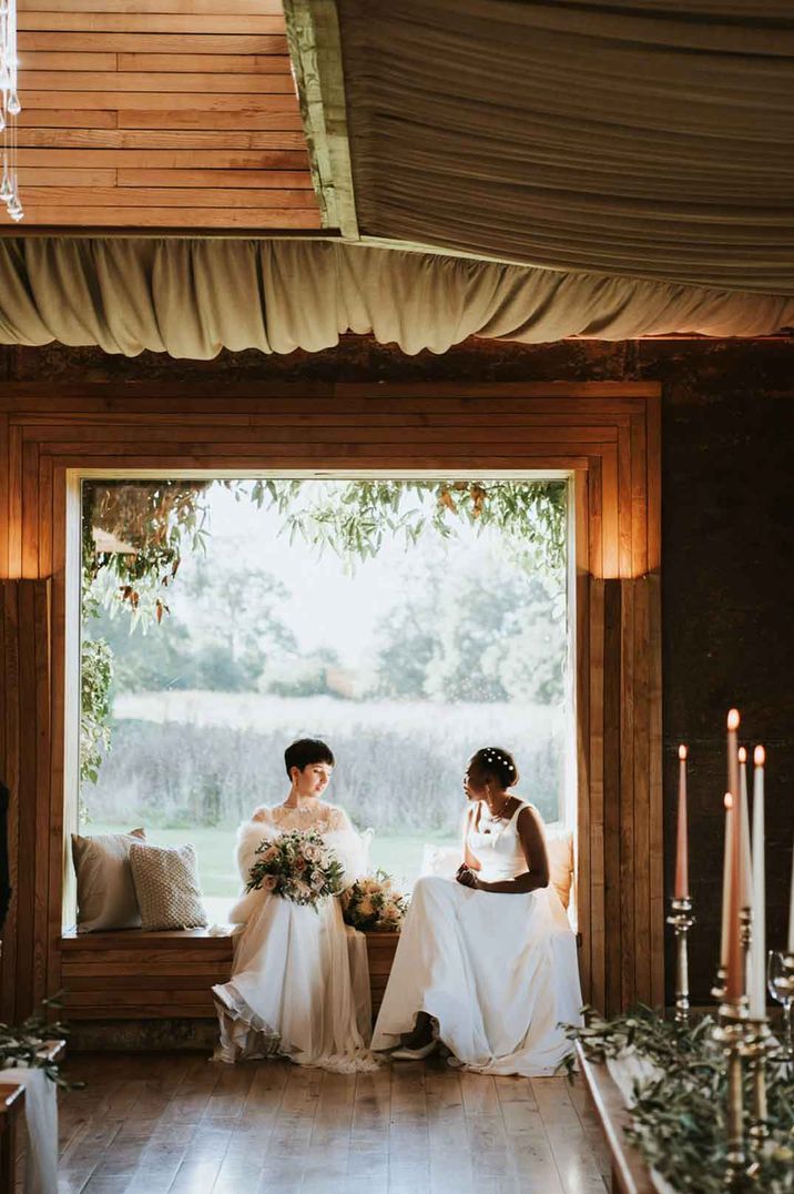 Brides in complimenting ivory wedding dresses sitting on the windowsill seat at Elmore Court country house wedding venue search