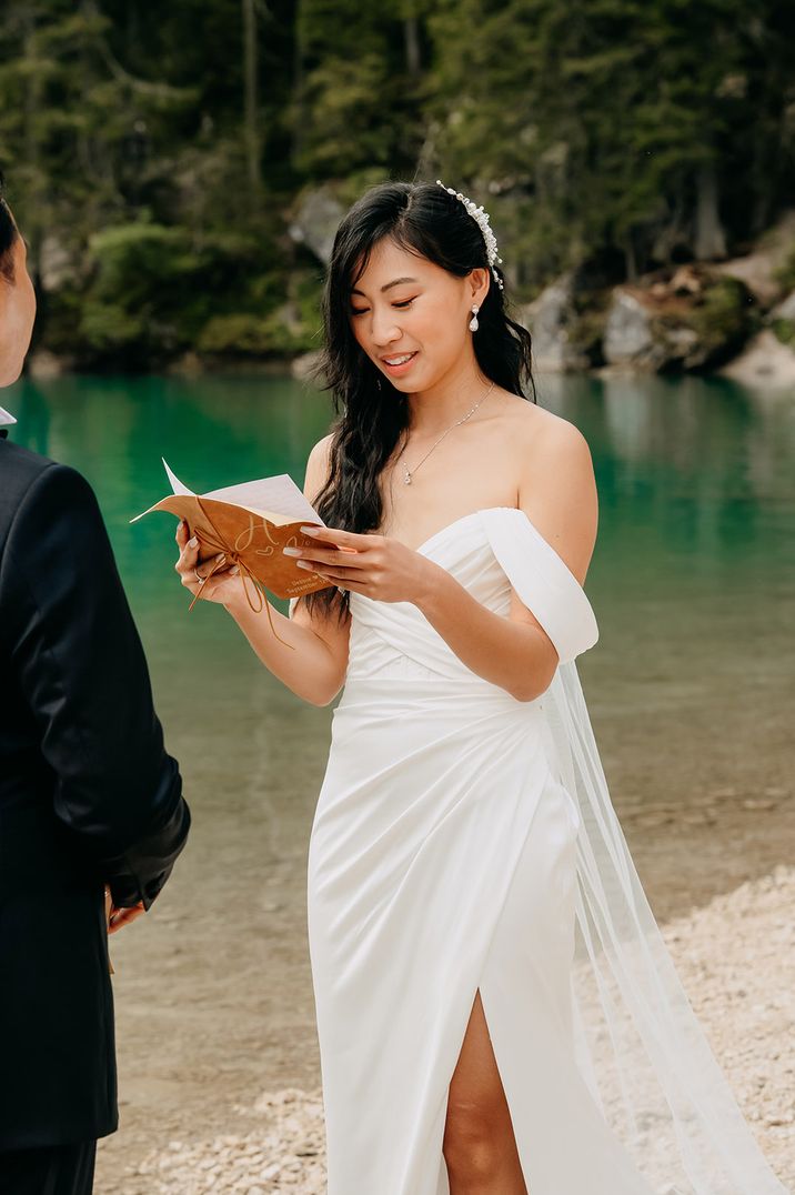 Bride in off the shoulder wedding dress holds a wedding vow booklet as she reads them out at her wedding ceremony 