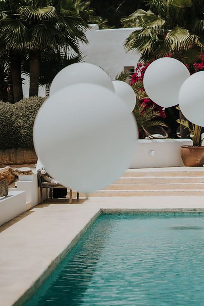 Outdoor swimming pool with large white decorative balloons for Ibiza wedding by Balti Rėmeliai