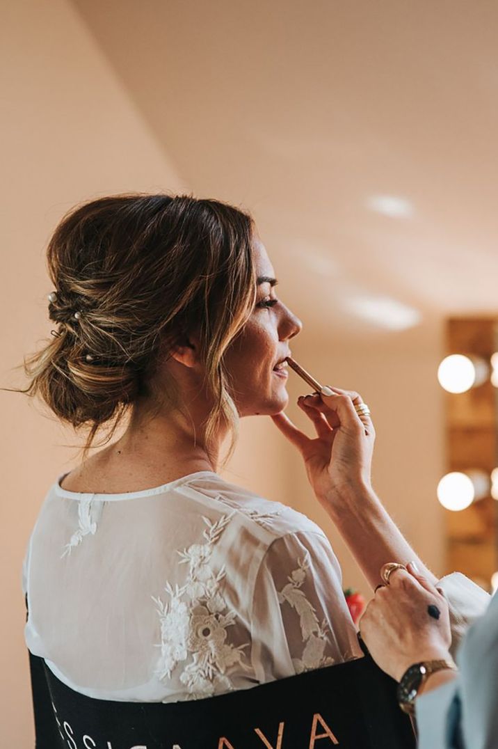 Bride sits facing light up mirror with hair in an elegant bun updo 