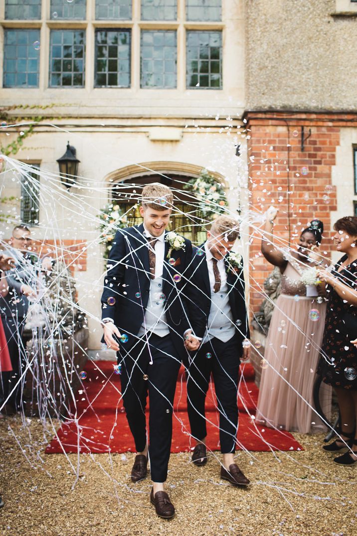 Two grooms in matching dark blue suits with confetti and silly string