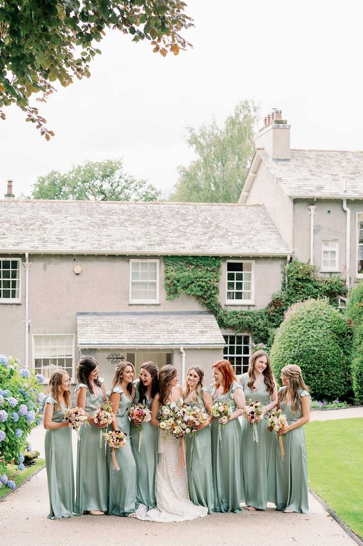 Eight bridesmaids in light green satin butterfly sleeve dresses with bride in strapless boho wedding dress 