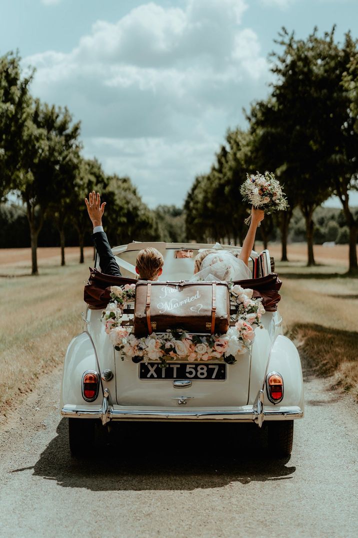 Convertible white wedding car with rose heart wreath and "just married" suitcase decoration on trunk