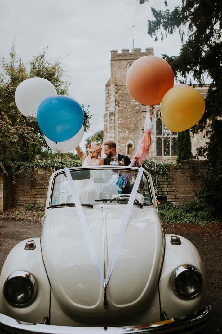 Classic convertible wedding car with white ribbon and large colourful balloons 