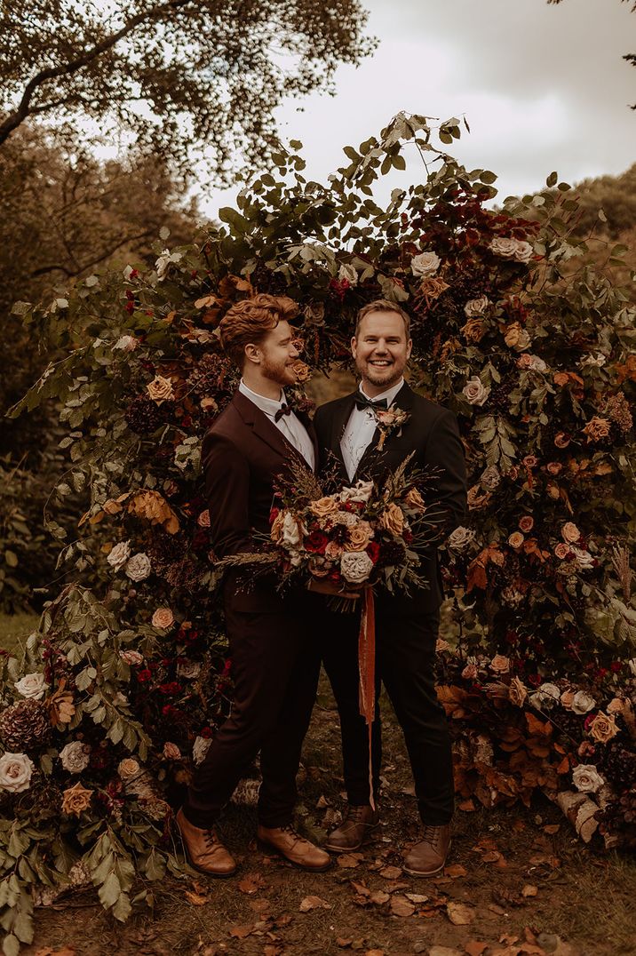 LGBTQIA+ wedding with two groom standing in front of flower arch autumn wedding decoration for the altar 