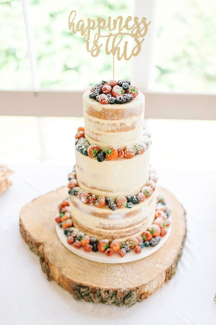 Three tier white semi naked wedding cake with red berries around the edges of the cake with personalised wedding cake topper 