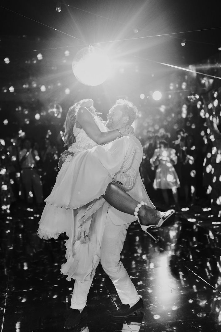 The groom lifts the bride up in epic lift caught perfectly by the light and disco ball 