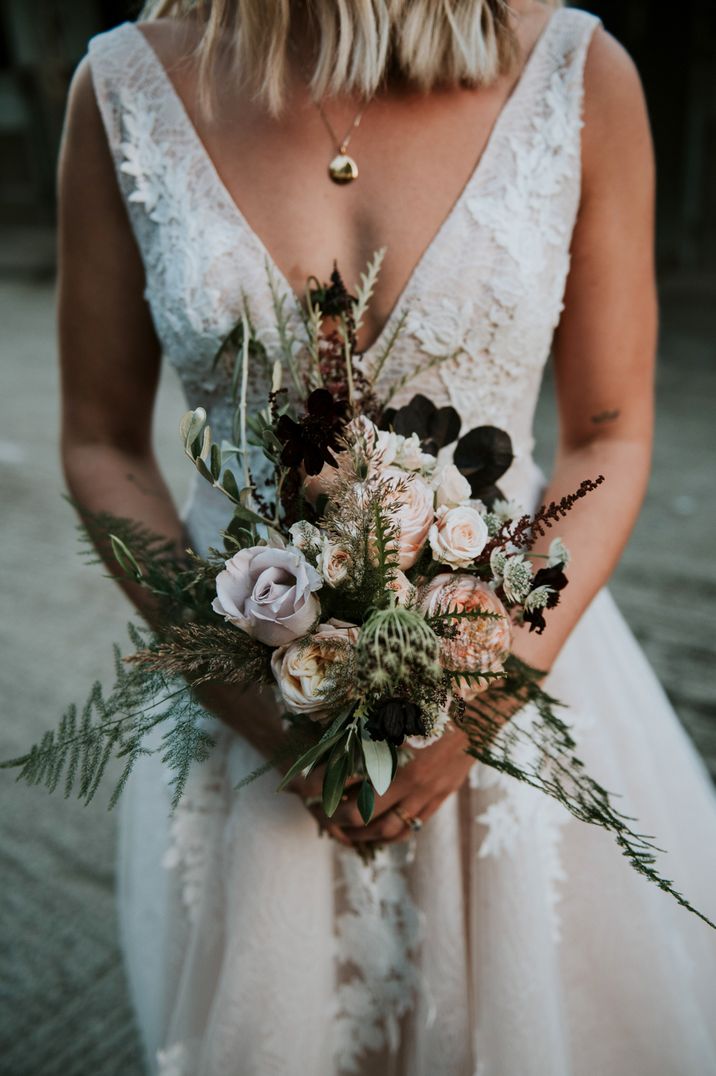 Bride in a lace wedding dress holding a peach and lilac rose bouquet with foliage 