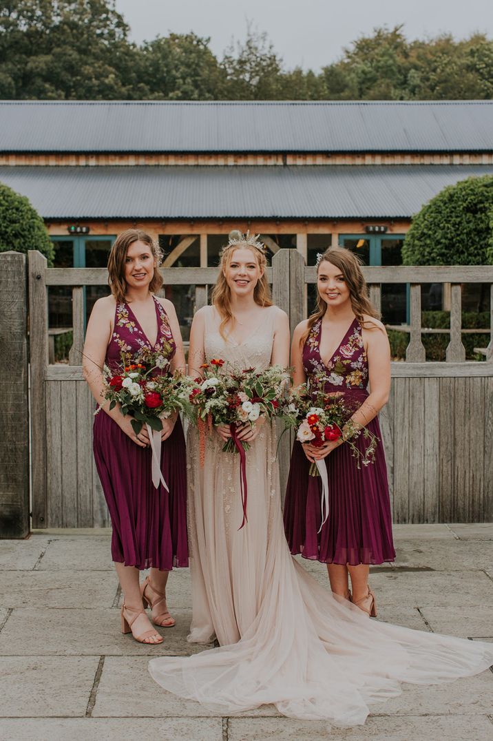 Rustic wedding with bride in a blush pink dress and crown and bridesmaids in short burgundy bridesmaids dresses with embroidered detail