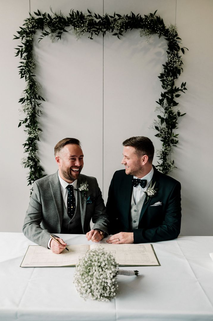 Grooms signing the register with greenery foliage backdrop 