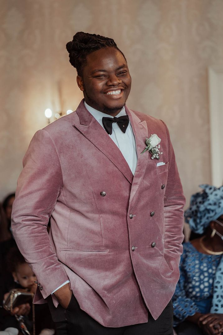 Groom in a dusky pink velvet suit jacket with a black bow tie and white rose buttonhole 