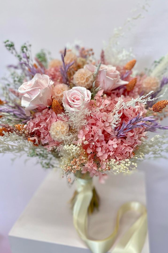 Pretty pink preserved flower bridal bouquet with pops of purple and orange tied with cream ribbon 