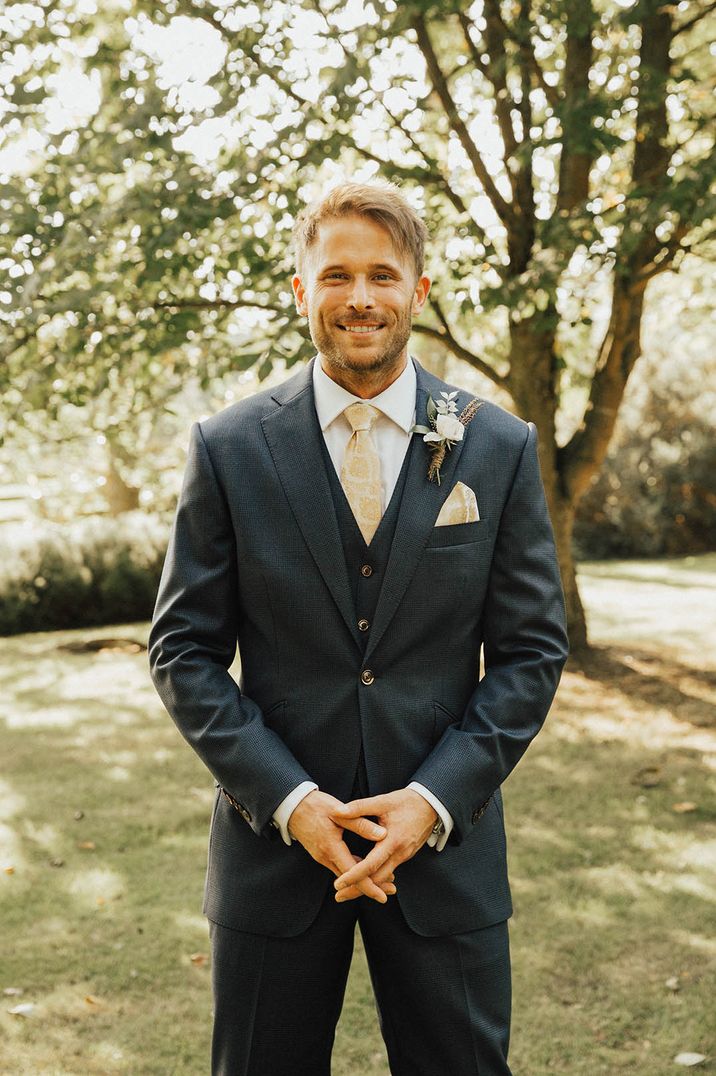 Groom in three piece navy suit with a white and yellow patterned tie and pocket square for Tythe Barn wedding 