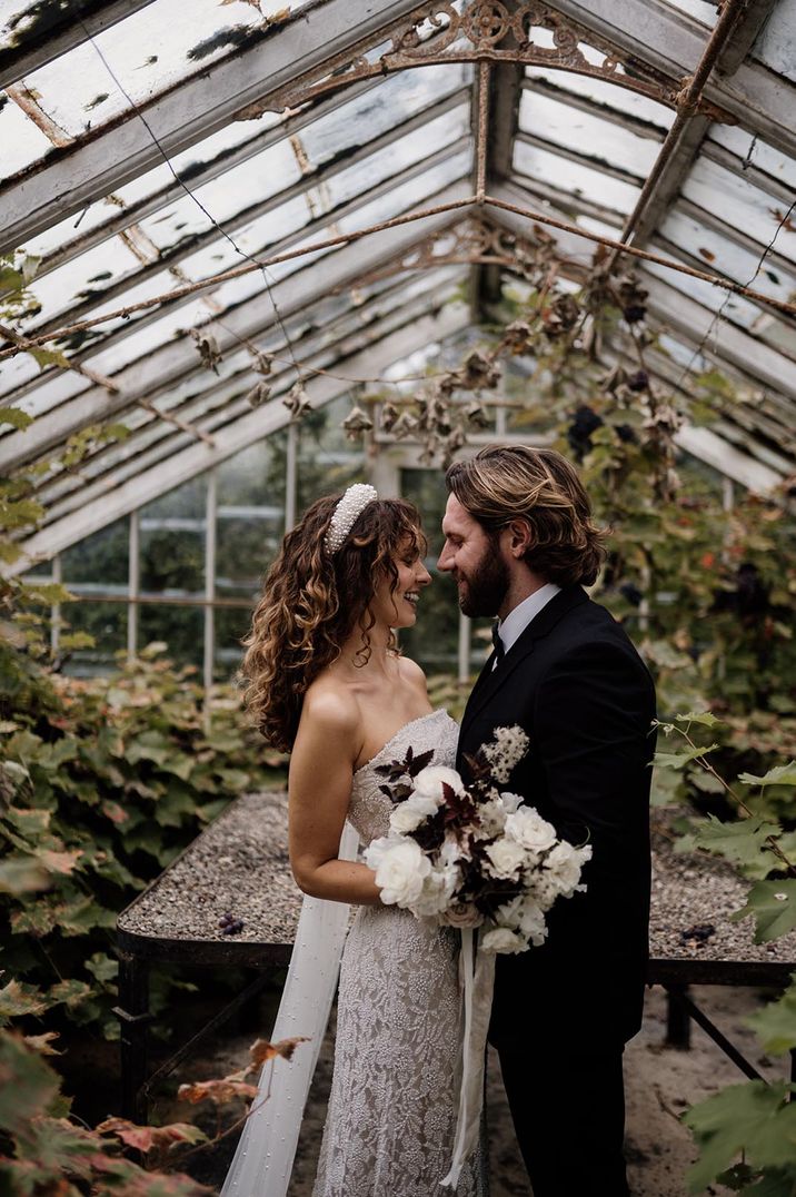 Bride in strapless lace wedding dress and pearl headband and groom in dark tuxedo embracing at Plas Dinam Country House glasshouse wedding venue 