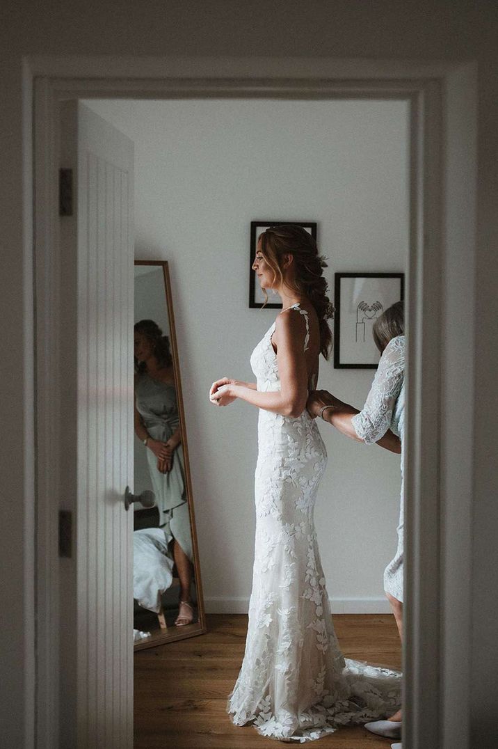 Bride in bodycon sleeveless lace wedding dress getting help from her bridesmaid - timeline of wedding day 