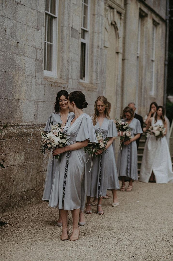 The bridesmaids in grey satin metallic dresses preparing to walk down the aisle for the country house wedding 