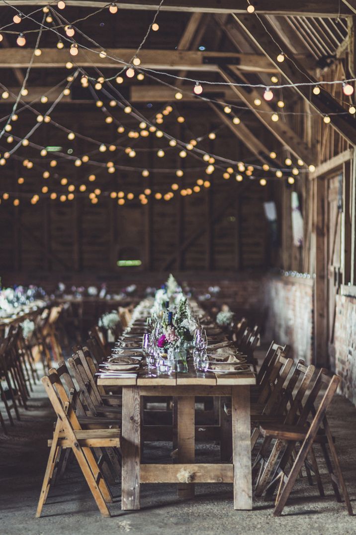 Rustic wedding reception with hanging festoon lights and wooden tables 