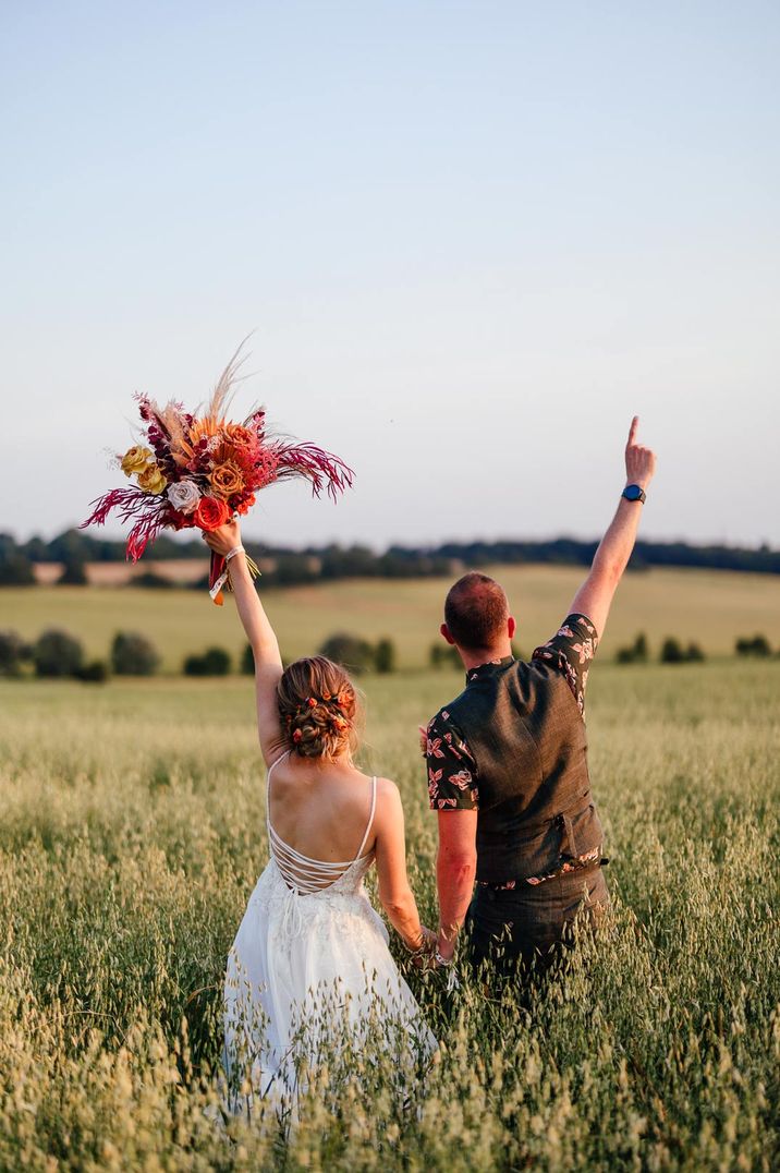 Bride in corset back wedding dress holding vibrant floral bouquet and groom in patterned shirt and waistcoat 