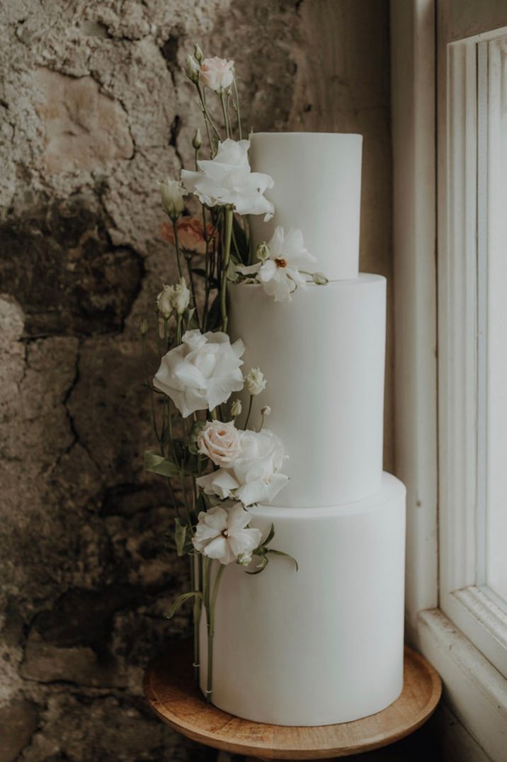 Tall three tier white frosted wedding cake decorated with white and green flowers 