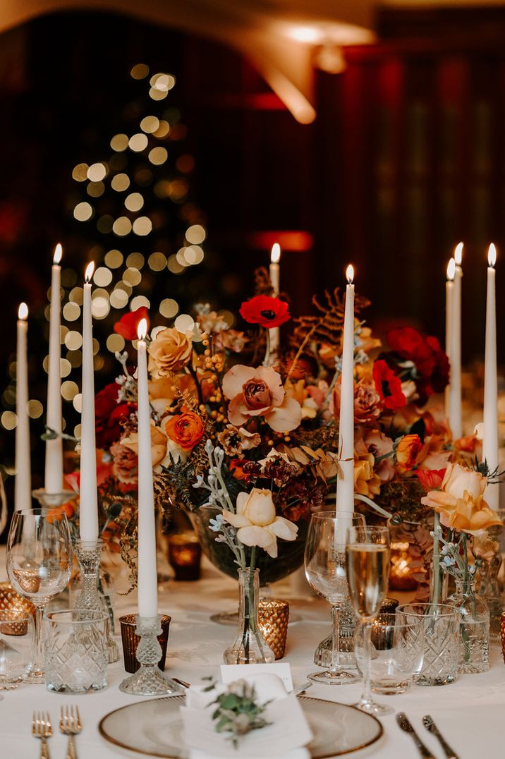 Orange and red warm toned wedding flowers with taper candles table centrepiece 