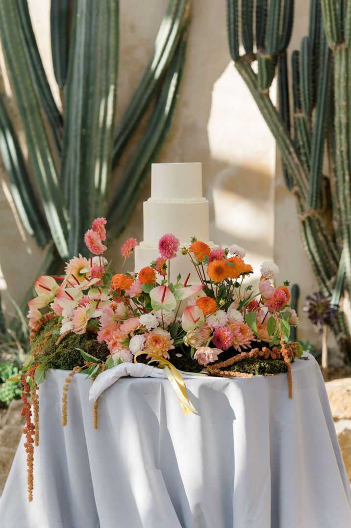 White iced wedding cake surrounded by colourful wedding flowers for vibrant 60k wedding 