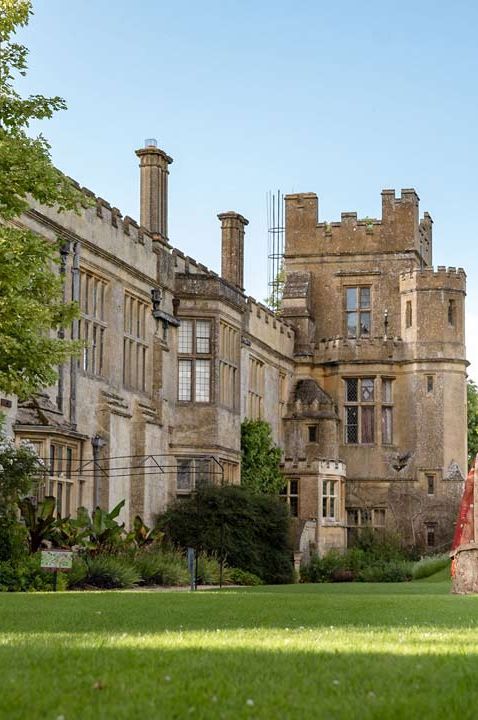 Bride and groom in traditional Indian wedding garments walking around the exterior and manicured lawns and grounds of Sudeley Castle wedding venue  