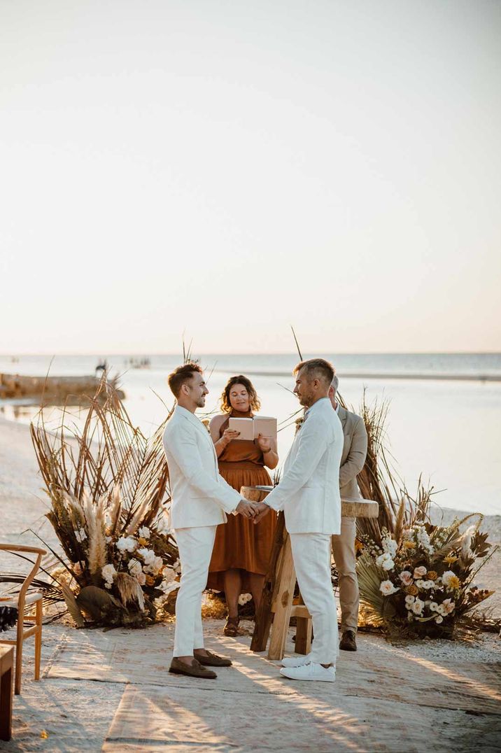 Grooms in matching mens white wedding suits at the end of the alter at Mexico destination wedding 