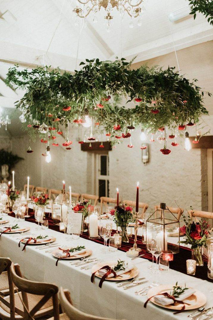 Long banquet table with white tablecloth, red velvet table runner and red taper candles at Christmas wedding 