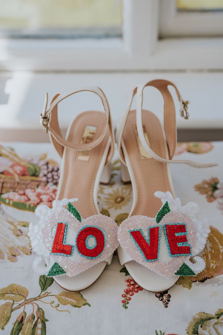 White wedding shoes with sequin decal spelling out love in the shape of a heart 