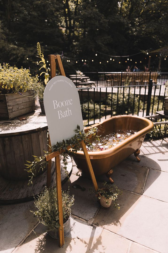 Neutral wedding signage next to bath filled with ice and cans of drinks for guests 