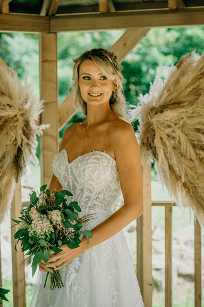 Bride in strapless lace wedding dress holding white rose wedding bouquet with foliage 