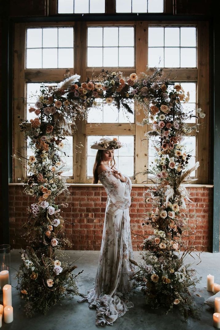 Bride in long embroidered white wedding dress standing under white floral arch at The Giraffe Shed wedding venue