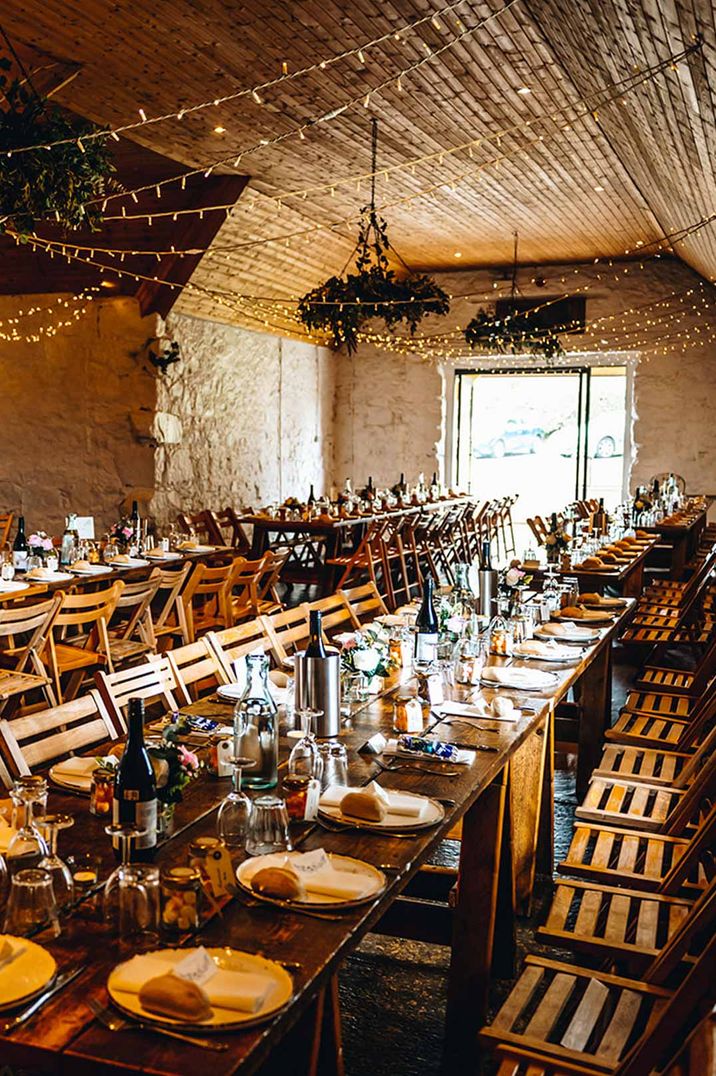 Classic warm rustic wedding tablescape at Dalduff Luxury Barn wedding venues Scotland with fairy lights and suspended foliage decorations 