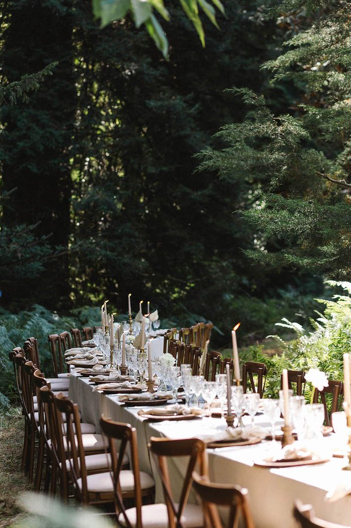 Outdoor woodland wedding tablescape with white tablecloth and candles 