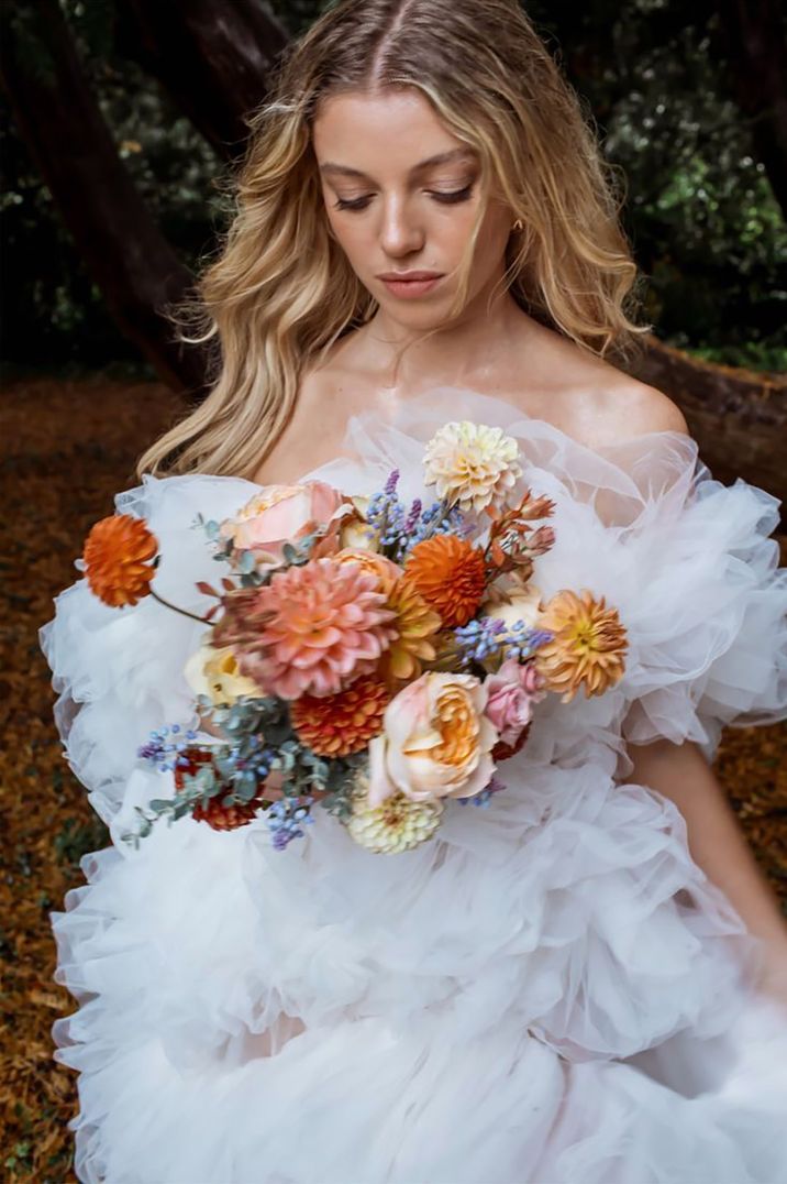 Bride in off the shoulder wedding dress with pastel dahlias in different shades 