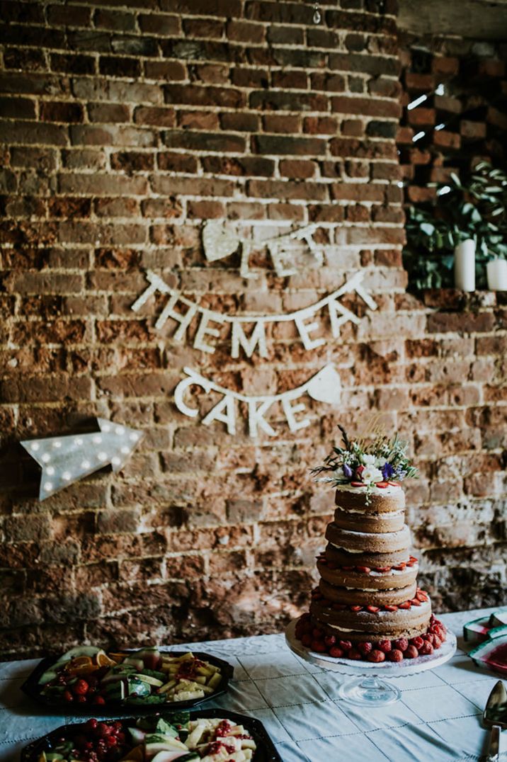 Dessert table with naked sponge wedding cake and bunting sign on the wall 