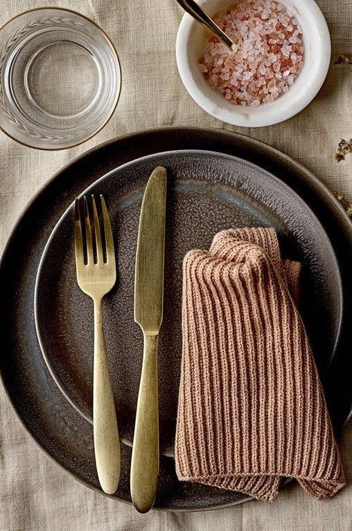 Gold cutlery with black plate and pink napkin