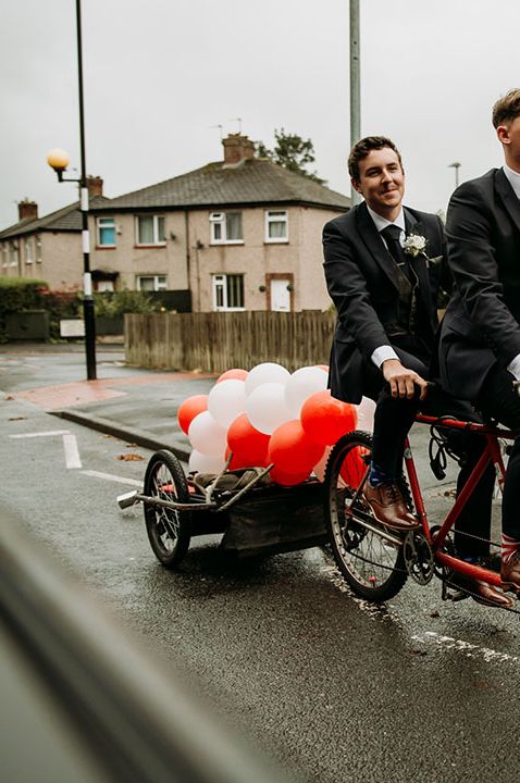 Men on tandem bike in matching black suits with red and white balloons decorations