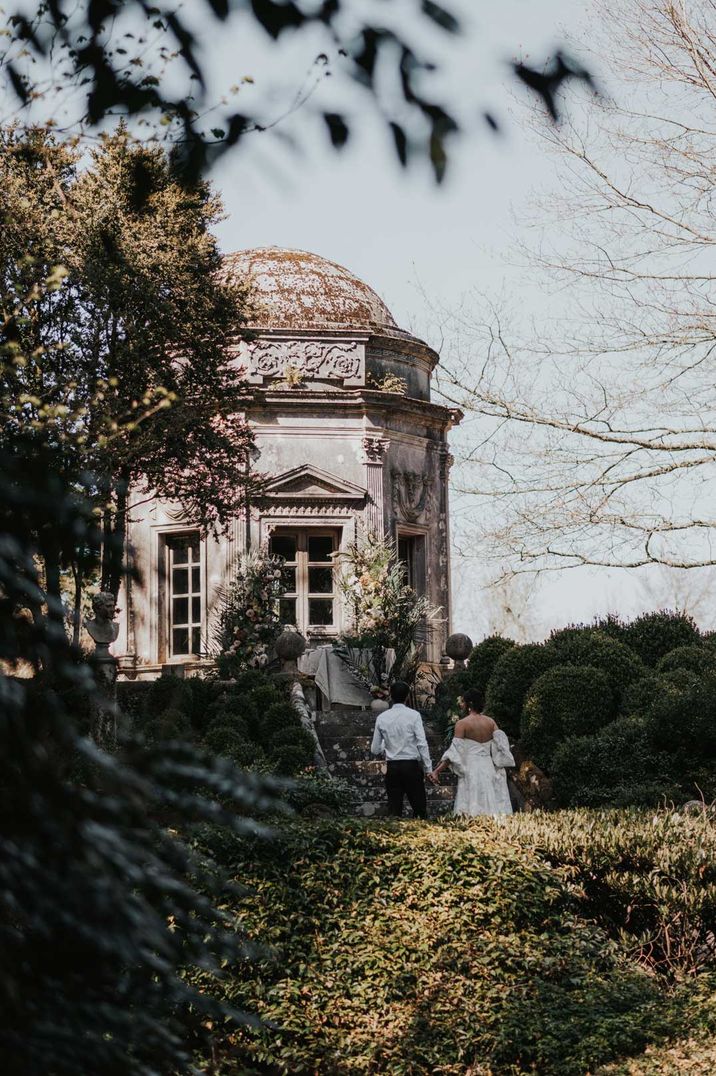 Bride in off the shoulder puff sleeve wedding dress and groom in white shirt and suit trousers at Larmer Tree Gardens