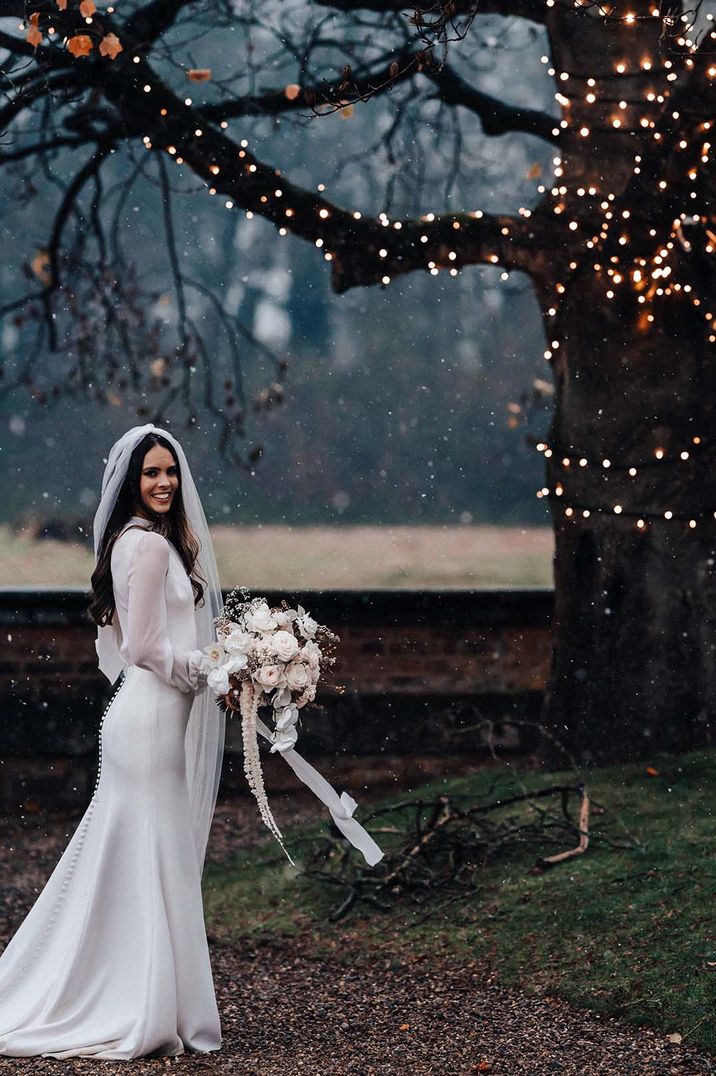 Bride poses for her winter wedding with long sheer sleeves and button back detail 