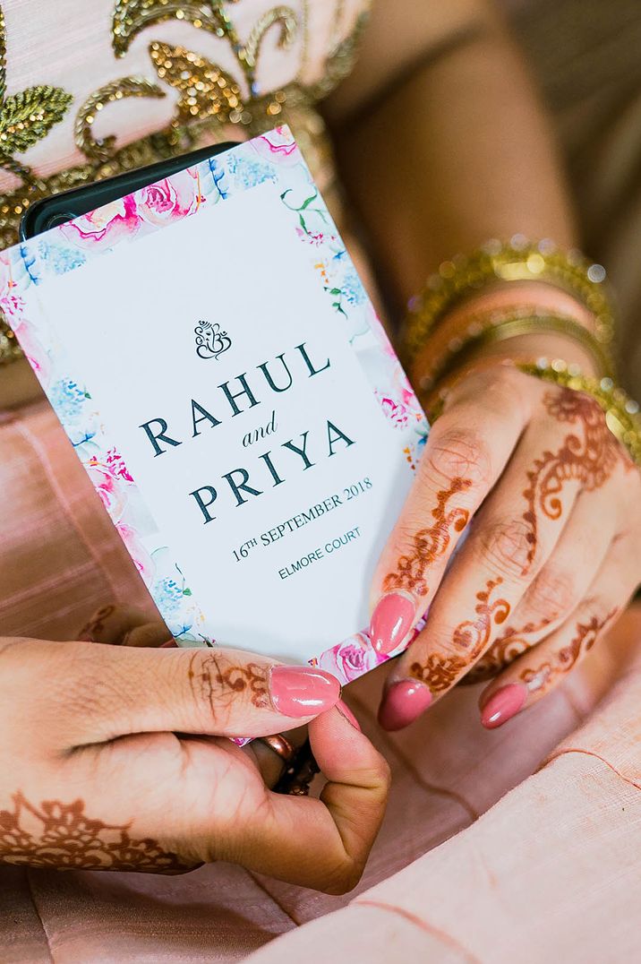 Bright coloured wedding stationery held by bride with pink almond shape nails with henna for wedding under 40k 