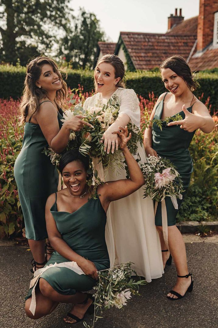 Bridesmaids in forest green slip bridesmaid dresses standing with bride in long sleeve lace wedding dress 