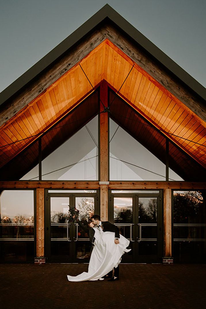 The bride and groom pose in front of the winter wedding venue 