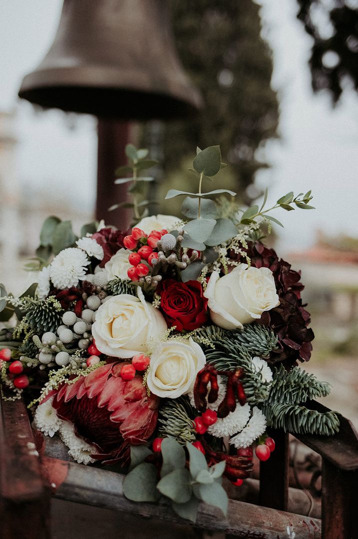 Red and white winter wedding bouquet with roses, dahlias, king proteas, hydrangeas, evergreen leaves and more 