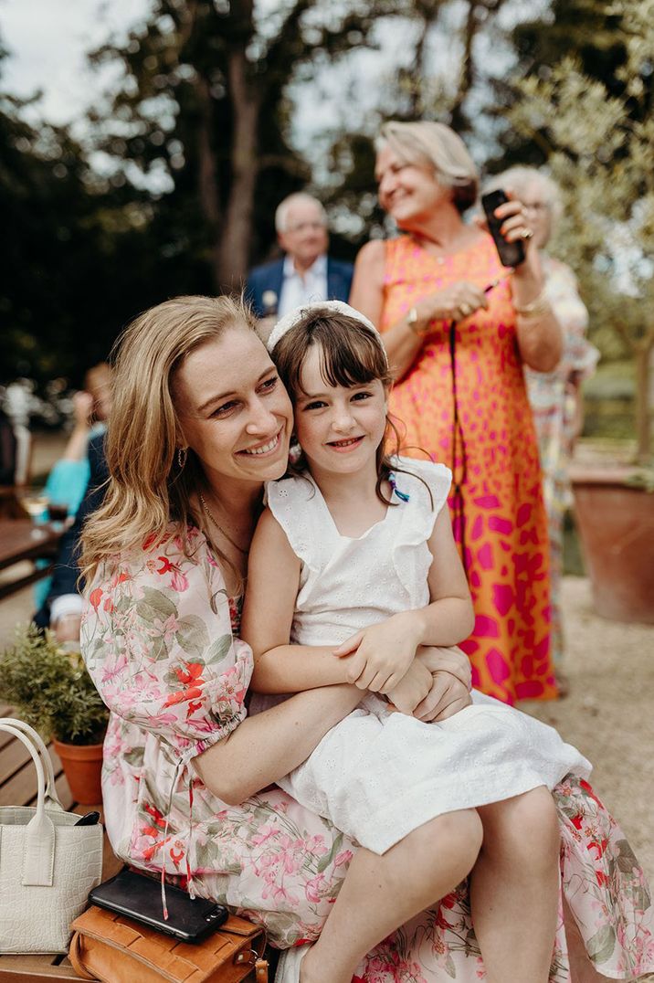 Wedding guest wearing a floral dress smiling with a child sitting on her lap 